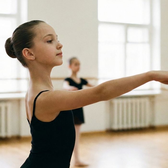ballerina in a leotard and bun gracefully extends her arm during a ballet class