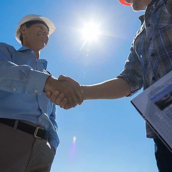 two smiling men wearing hard hats shaking hands