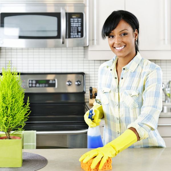 Smiling woman using a sponge and cleaning solution to clean countertops. 