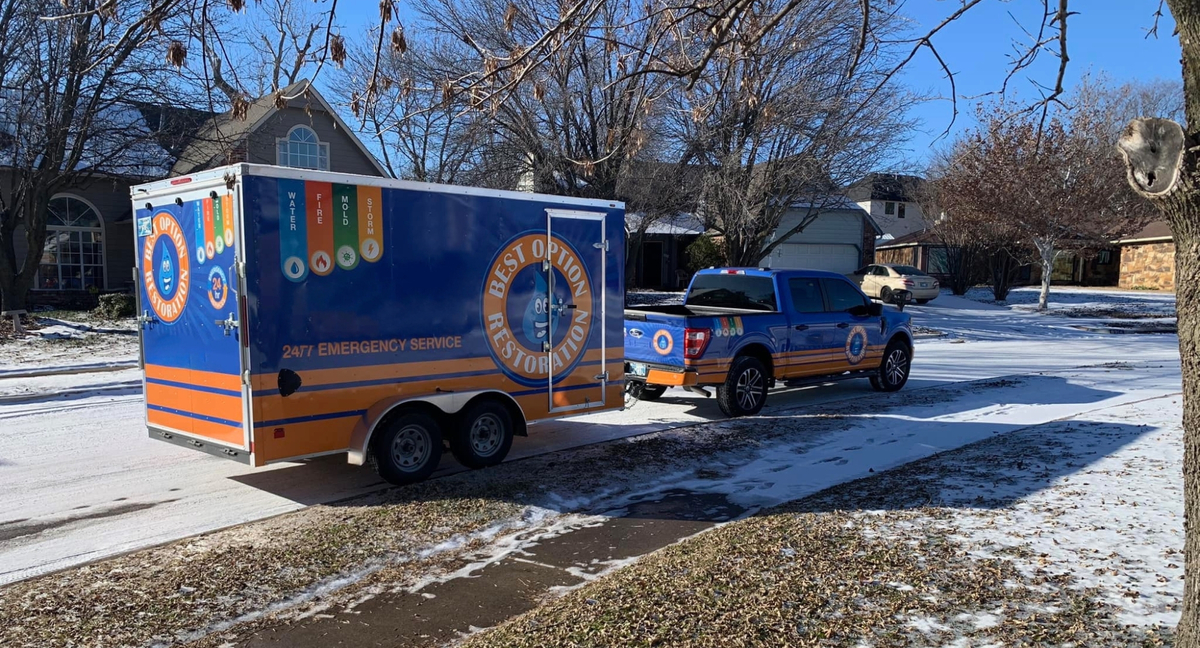 A branded Best Option Restoration truck and trailer driving through a snowy residential neighborhood.