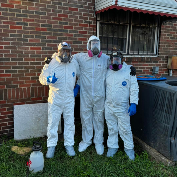 Three restoration professionals wearing full white protective suits and respirator masks standing outside a brick home.
