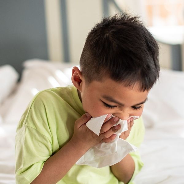 little boy sneezing into a tissue