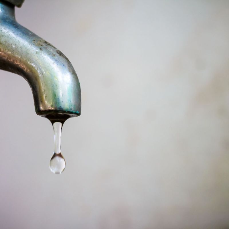A single, clear drop of water falling from the tip of a weathered metal faucet.