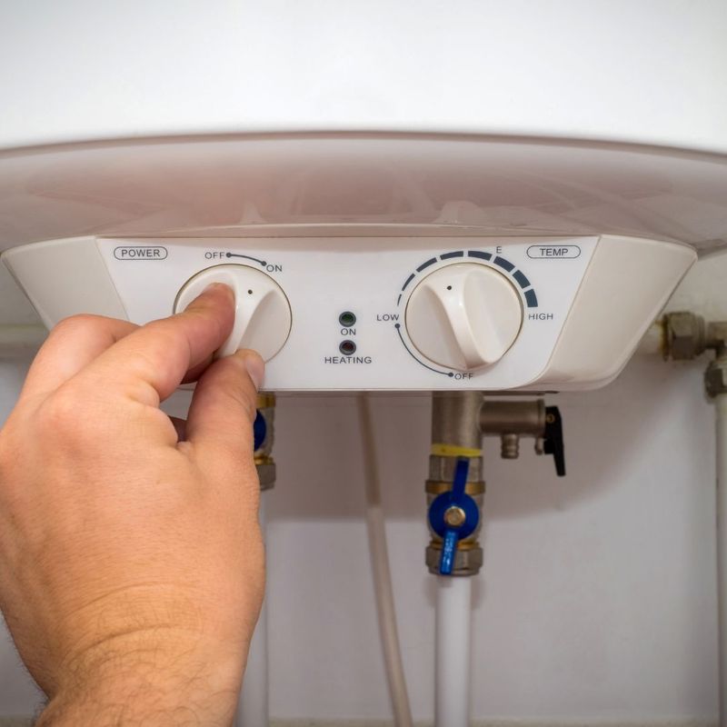A person’s hand adjusting the power dial on a white water heater unit.