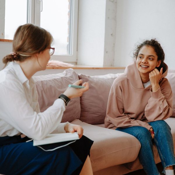 Two women smiling and conversing on a sofa