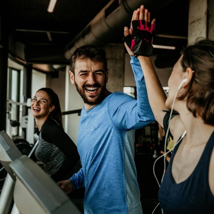 Group of smiling friends on treadmills giving high fives 