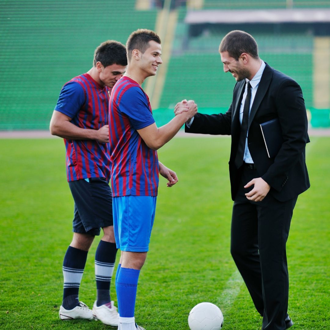 Man in a suit shaking a soccer player's hand. 