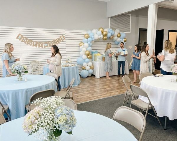 An elegant baby shower celebration featuring a blue, white, and gold balloon arch and circular banquet tables.