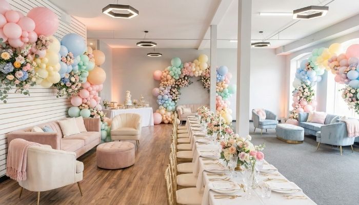 Bright and airy baby shower venue setup featuring pastel balloon arches, elegant floral centerpieces, and white table linens.