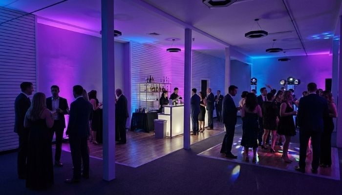 Modern adult birthday party celebration in a venue with dramatic purple and blue atmospheric lighting and socializing guests.