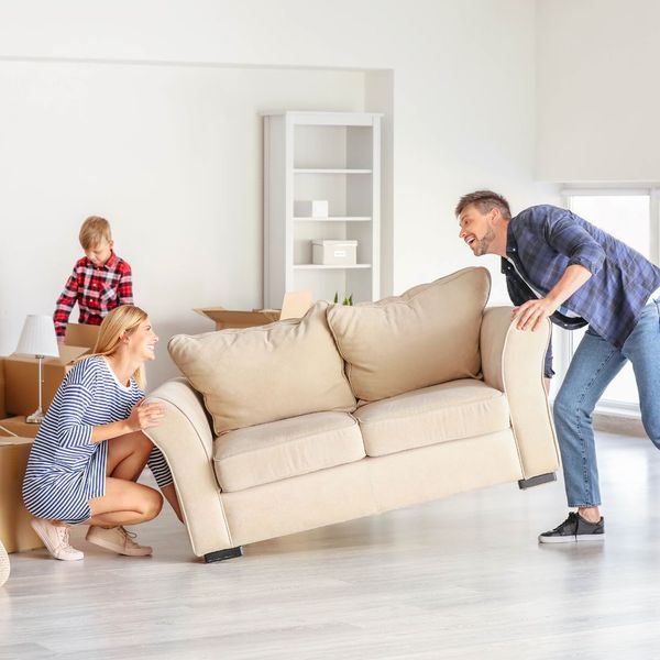 2 adults lifting a couch while a child packs boxes in the background
