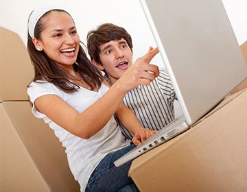 Young people smiling using a laptop surrounded by moving boxes
