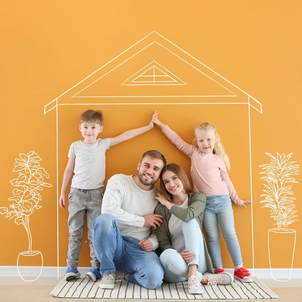 A couple of adults and 2 children sitting in front of an orange wall with a house drawn on it