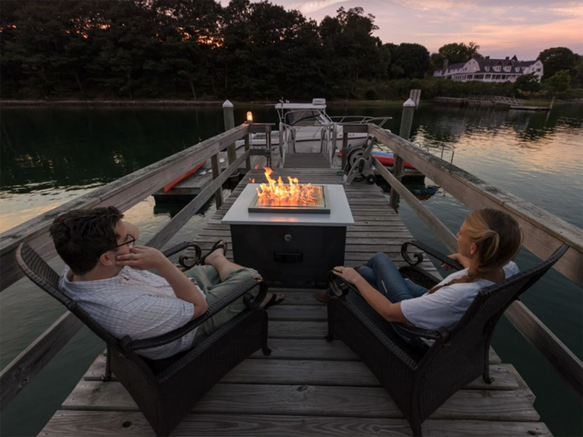 Image of a couple relaxing near a fire pit, on a dock over a lake.