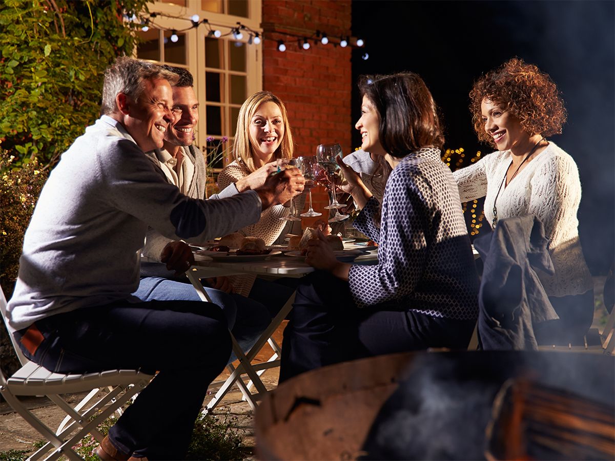 Image of a group of friends enjoying an outdoor meal near a fire pit.