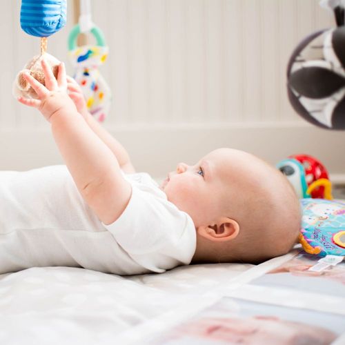a baby playing on a blanket with a toy mobile