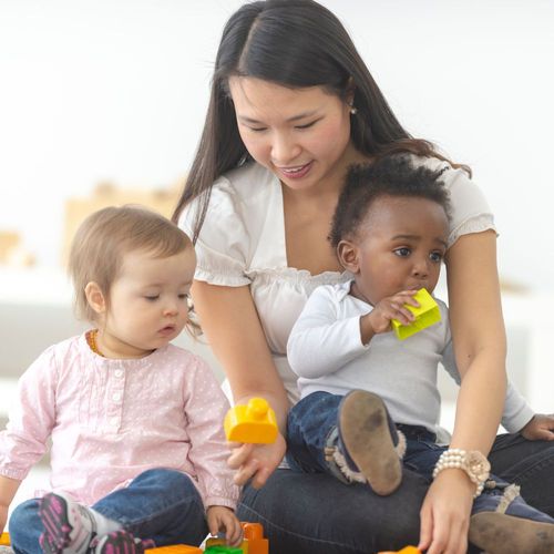 a daycare worker playing blocks with two infants