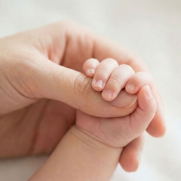 A close-up photograph of a mother holding her baby's hand.