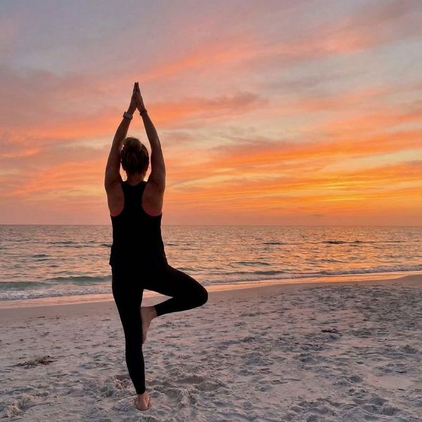 A woman in a yoga pose on a beach during a beautiful sunset.