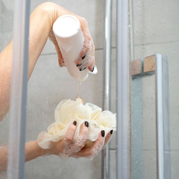 a woman putting soap on a loofa in the shower