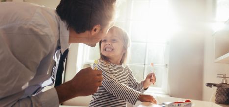 Father and daughter brushing teeth standing in bathroom and looking at each other