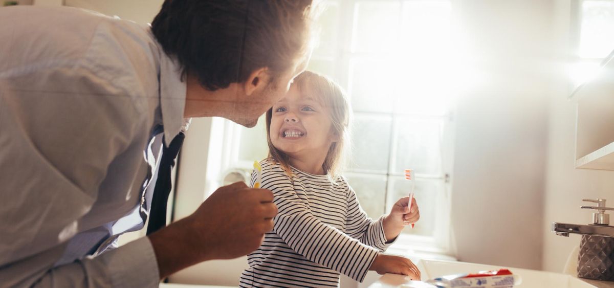Father and daughter brushing teeth standing in bathroom and looking at each other