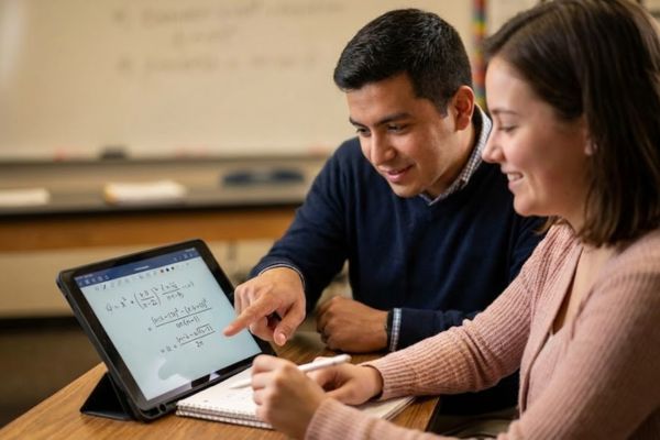 a teacher sitting with a student, pointing at a complex math equation on a tablet