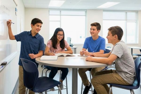 a small group of four diverse middle school students collaborating on a project around a round table in a modern classroom