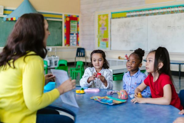 teacher holding up page for three students in classroom