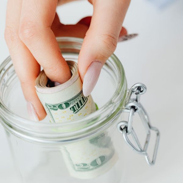 placing a rolled up stack of cash into a jar to signify savings