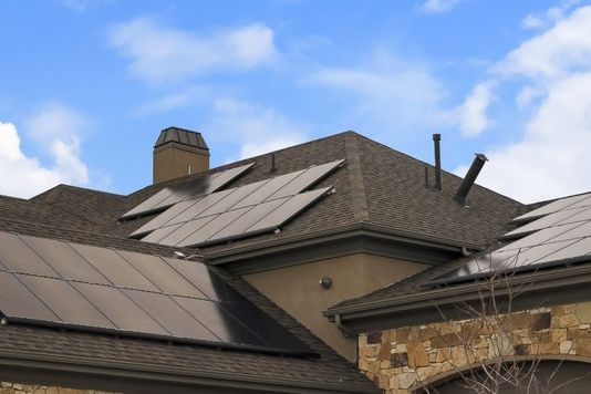 A modern home with sleek, black solar panels professionally installed on its dark shingle roof.