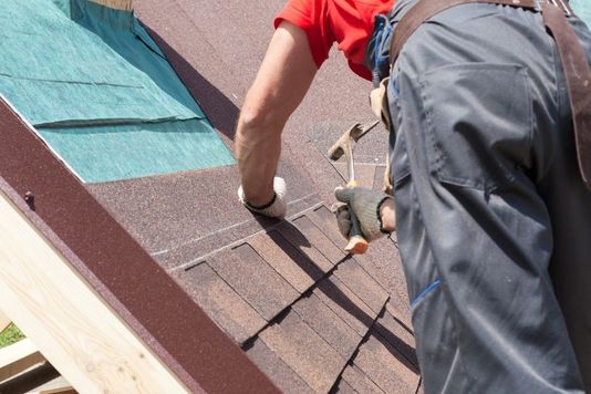 A roofer hammering a nail to secure an architectural shingle during a professional roof installation.