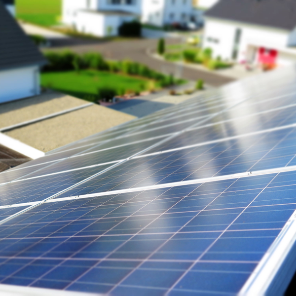 A close-up, angled view of solar panels installed on a residential roof, with a blurred background of a suburban neighborhood. A close-up, angled view of solar panels installed on a residential roof, with a blurred background of a suburban neighborhood.