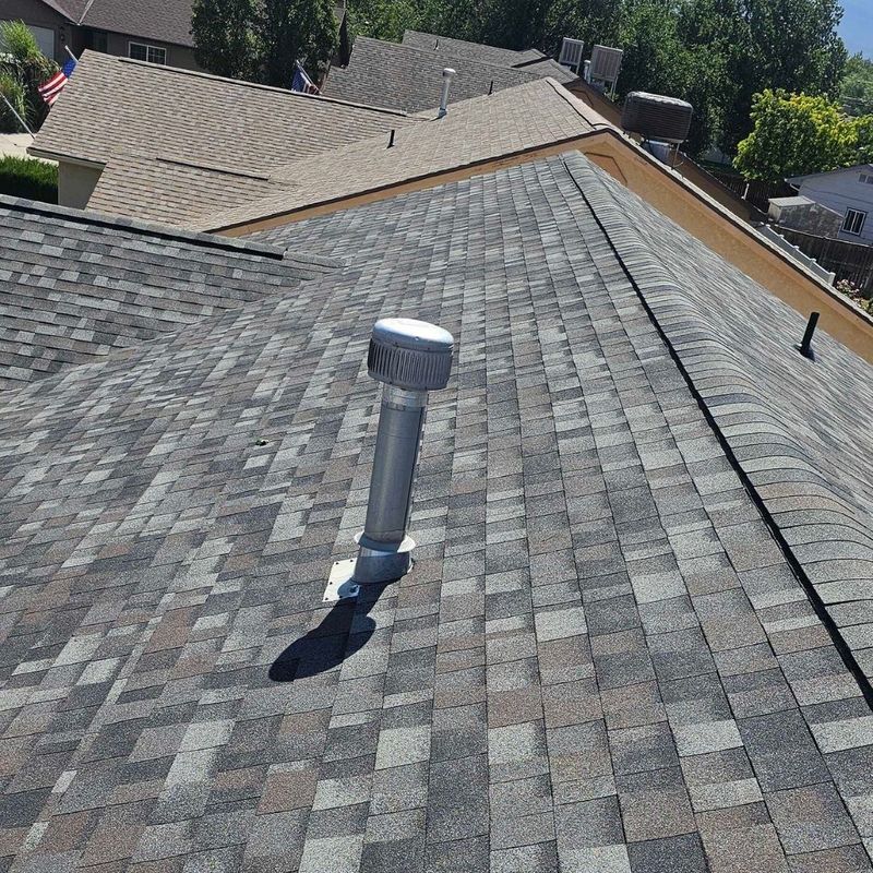 A newly installed architectural shingle roof with a modern color blend and a new silver vent pipe.