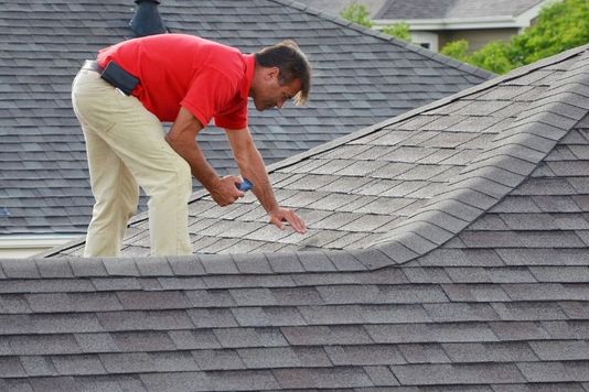 A roofing inspector carefully examining the condition of asphalt shingles on a residential roof.