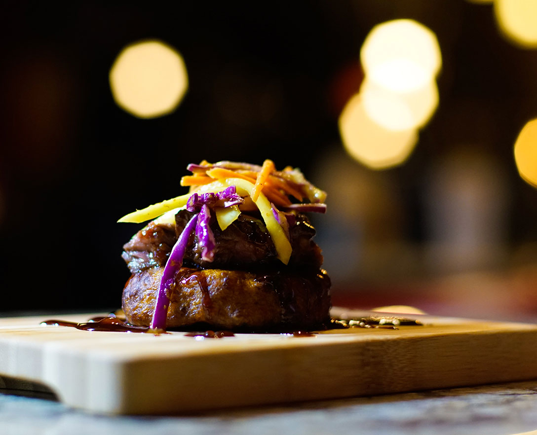 Side view of a cut of meat topped with vegetable slaw on a cutting board.