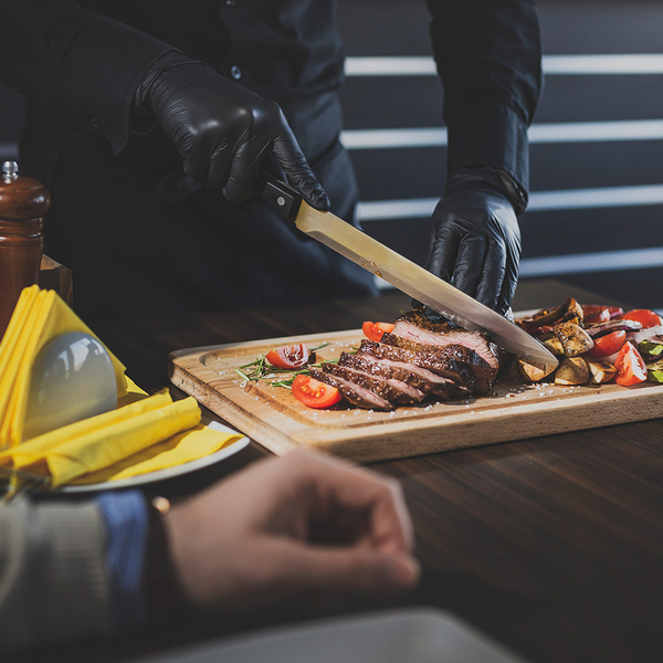 image of a chef slicing steak for a couple eating dinner