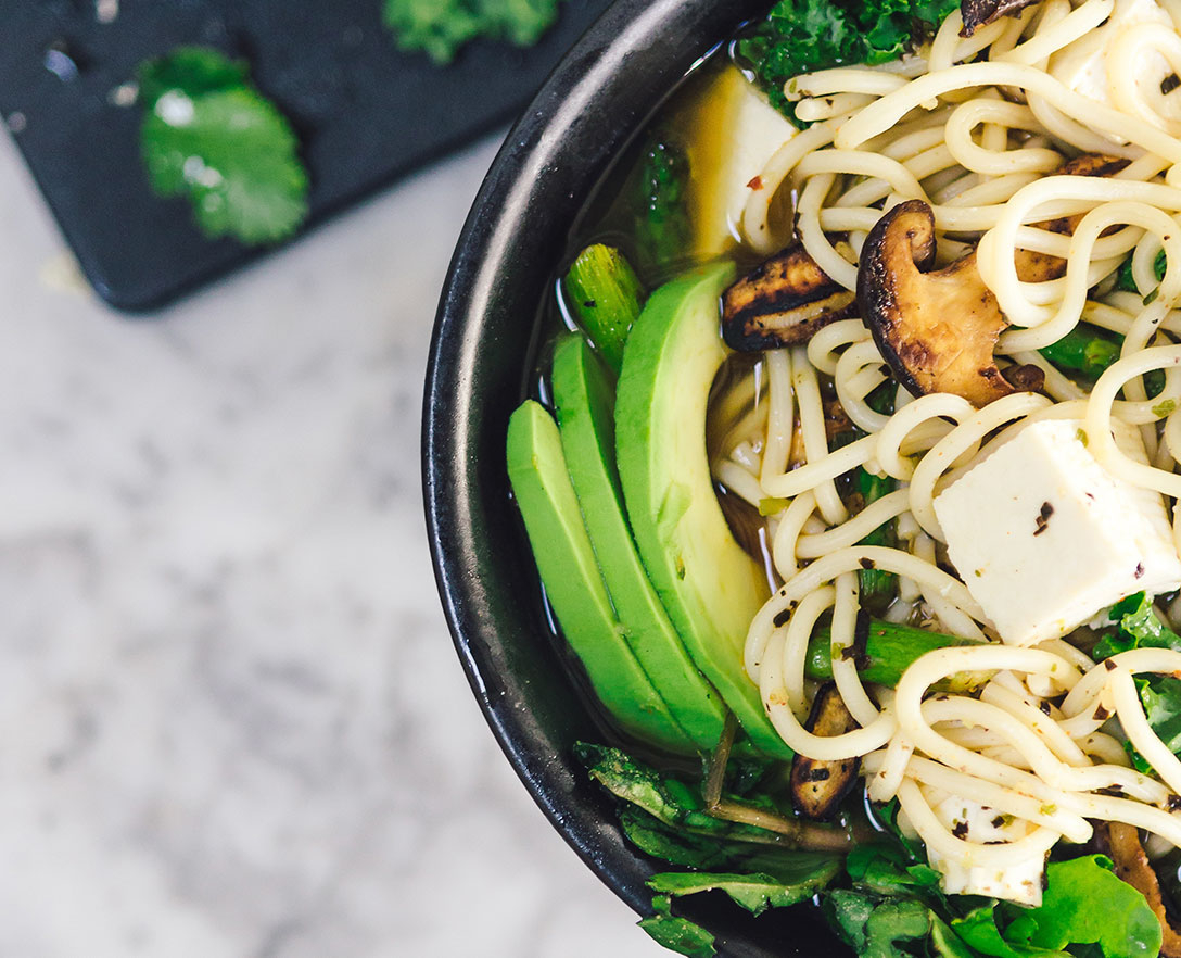 Zoomed in image of a bowl of noodles with tofu, avocado, and mushrooms.