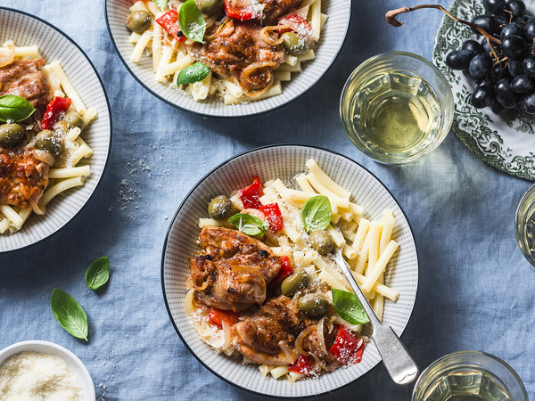 Italian food table. Pasta with slow cooker chicken with olives and sweet peppers, white wine. On a blue background, top view