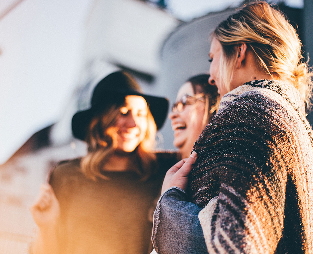 Three girls smiling together in a group outside.