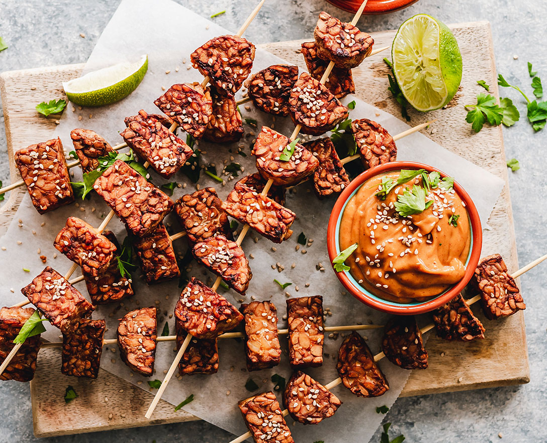 Aerial view of seasoned meat kabobs on wooden boards with lime wedges and a bowl of sauce.