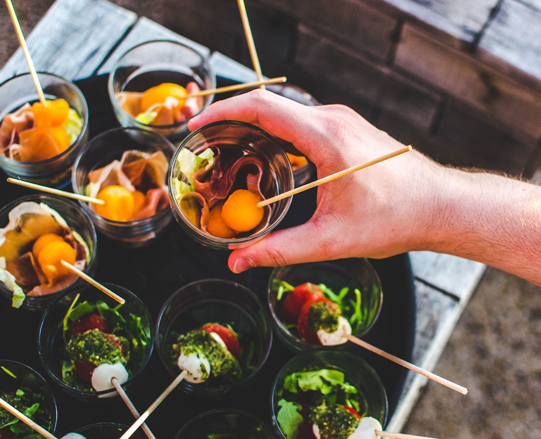 Hand grabbing an hor d'oeuvre dished in a small serving cup from a tray.