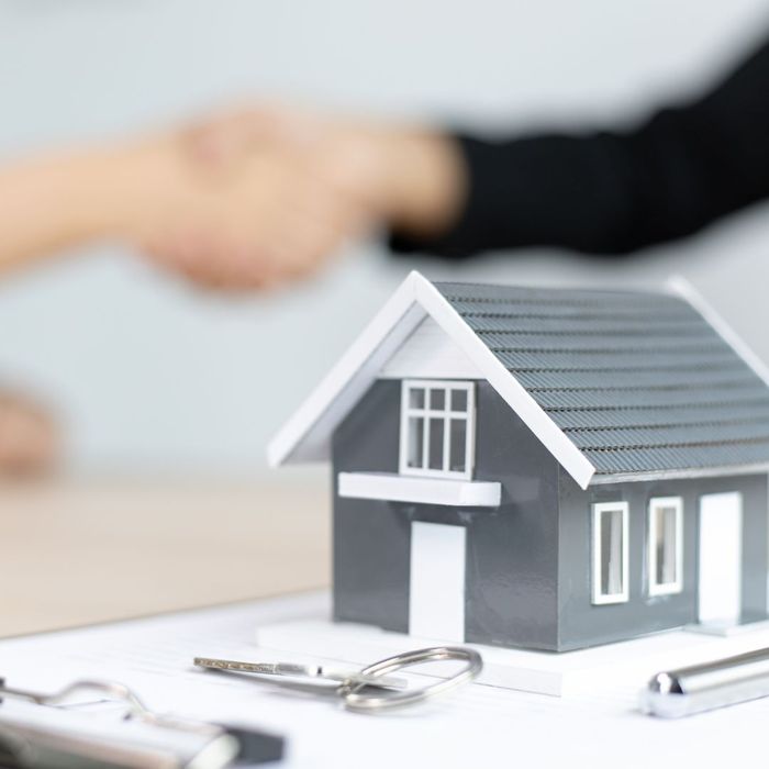 Small model of home sits on paperwork with people shaking hands in background