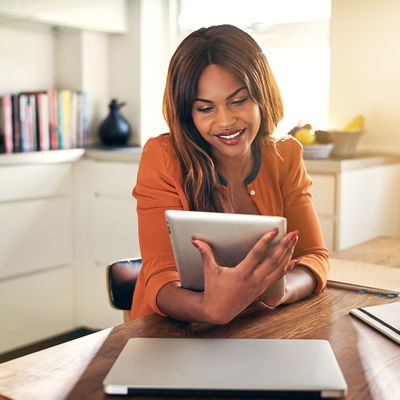 A woman sitting in her kitchen looking at her tablet