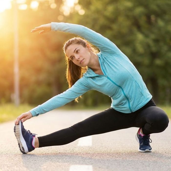 A woman in athletic wear stretches her arms toward the sky during a sunny outdoor morning jog on a paved path.