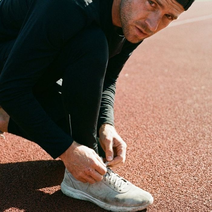A close-up of a man with a determined expression tying his running shoes, preparing for a workout with mental focus.
