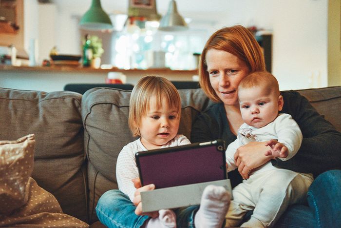 Woman sitting on the couch with two young children using a tablet