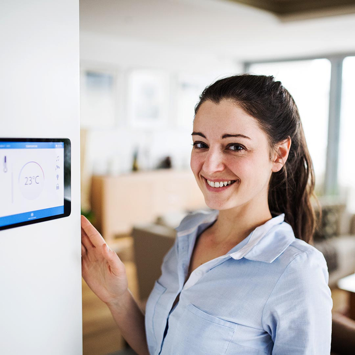 Happy woman standing next to a smart thermostat