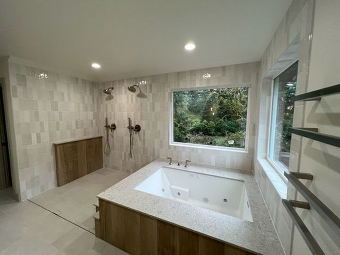 BKG Construction Group residential bathroom remodel with large bathtub, dual showerheads, modern wood paneling, recessed lighting, and luxury finishes designed and built by BKG Construction Group.