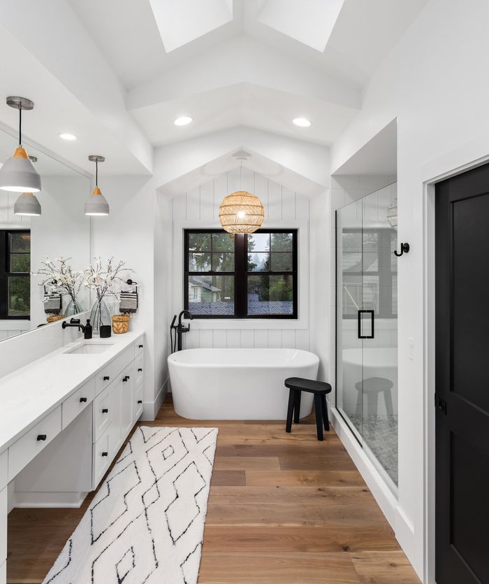 Modern bathroom remodel with white vanity, freestanding soaking tub, glass shower, and wood flooring by Stride Pro Builders.